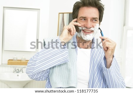 Smiling middle aged man shaving his face and speaking on cell phone