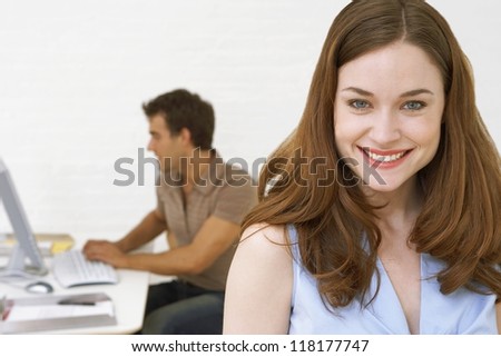 Pretty redhead businesswoman with a coworker working at a computer station behind her