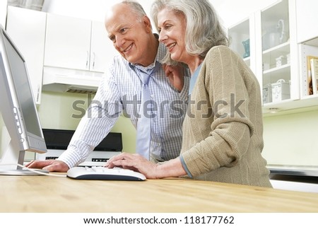 Senior retired couple at a desk using a computer and looking at the screen together