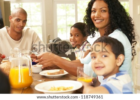 Happy young African American family seated around a table enjoying a healthy breakfast together in a relaxed start to the day