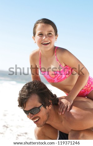 Little girl climbing up on dads shoulders for a tall ride during a fun day at the ocean