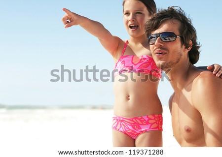 Little girl pointing out something of interest to her father looking down the beach