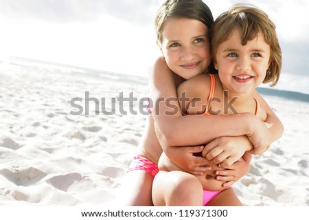 Little girl being hugged by her sister on sandy beach