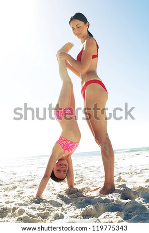 Young mother holds her daughters feet to prevent her falling as she does handstands on the beach