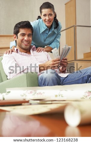 Low angle view of a young couple sitting in an armchair looking at home decor fabric and paint samples
