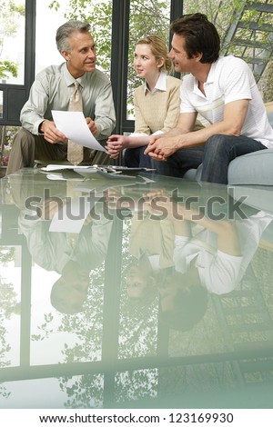 Salesman or investment advisor sitting with clients giving a presentation at the end of a reflective glass topped table