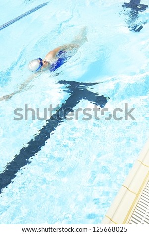 person wearing swimming cap and goggles, swimming freestyle in the swimming pool