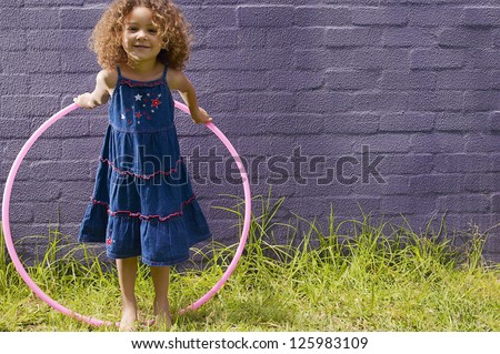 Cute little girl with curly hair posing with her hula hoop in front of a blue brick wall