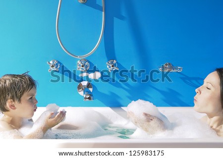 A young girl and her little brother sitting up to their necks in bubbles in the bath have fun blowing bubbles at each other off their cupped hands