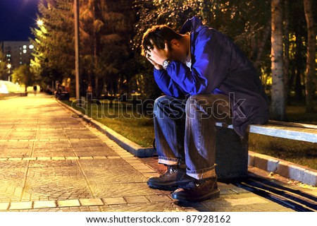 sad and lonely teenager with hidden face sitting in the night park