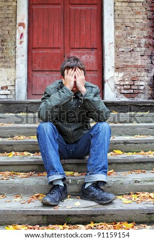sad young man with hidden face on the old house background
