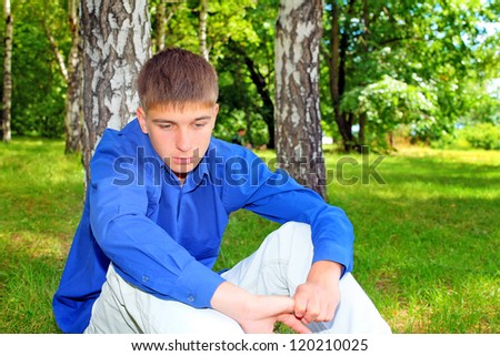 Sad Teenager sitting on the Grass in the Summer Park