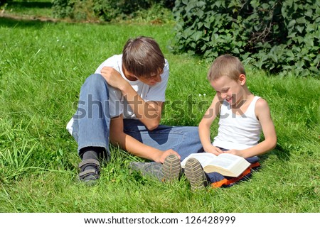 Older and Little Brothers reads a Book in the Summer Park