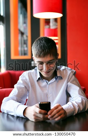 Cheerful Young Man Reading SMS on Mobile Phone at the Home