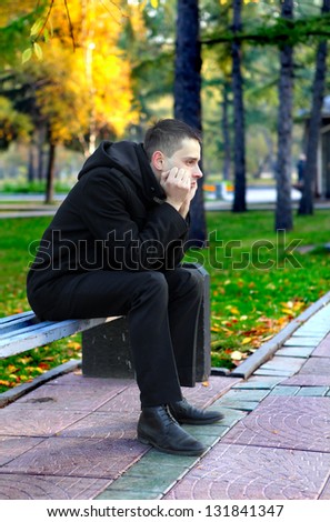 Sad young man sitting on the bench in the autumn park