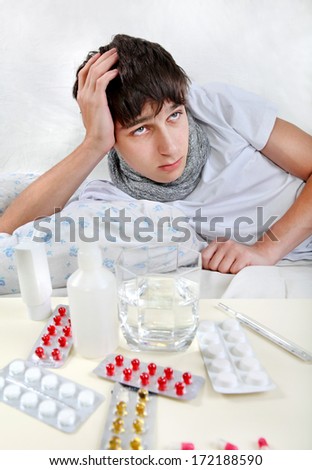 Sad and Sick Young Man lying on the Bed with Pills on foreground
