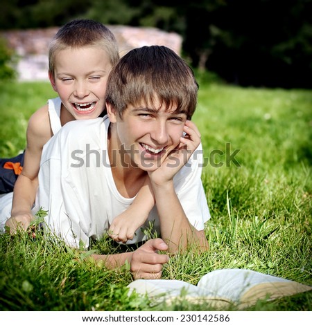 Happy Brothers lying on the Grass with a Book in the Summer Park