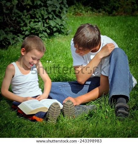 Teenager reads the Book to the Child in the Summer Park