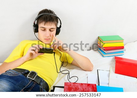Bored Student in Earphones with the Books on the Bed