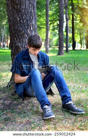 Teenager with Tablet Computer under the Tree in the Summer Park
