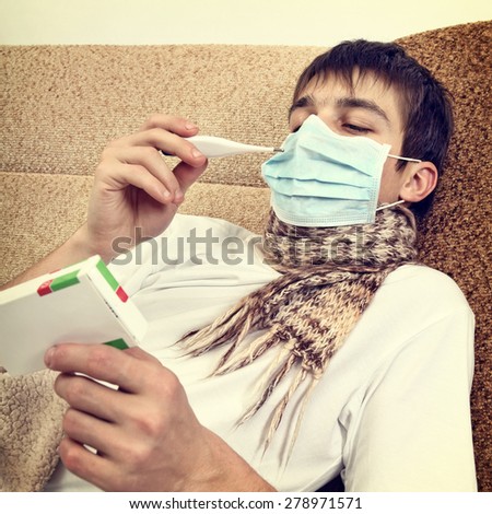 Toned Photo of Sick Young Man in Flu Mask with Thermometer at the Home