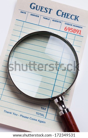 Guest Check and magnifying glass, concept of restaurant expense fraud.