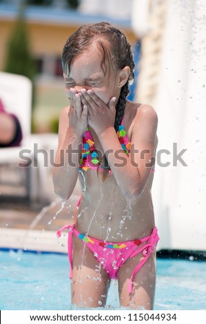 Happy little girl in swimsuit in pool at aqua park
