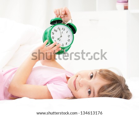 Beautiful little girl with alarm clock on bed in the bedroom