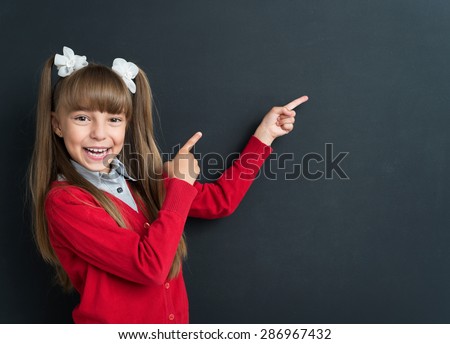 Little excited girl pointing at something at the black chalkboard in classroom.