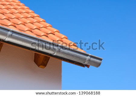 Corner of the house with gutters and ceramic tile roof on a background of blue sky.