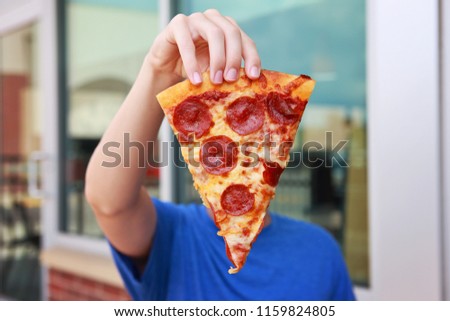 Boy holding a piece of pepperoni pizza in front of his face