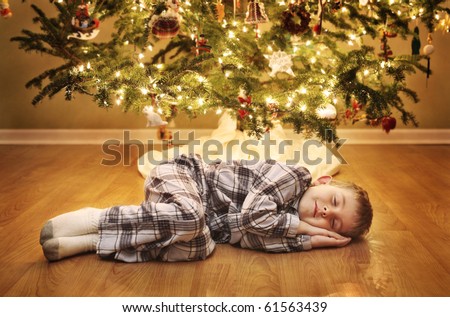 Young boy sleeping under the Christmas Tree waiting for Santa Claus to come