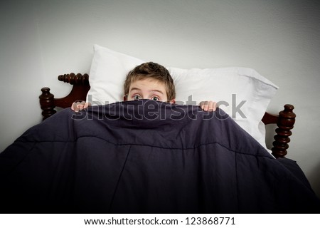 Boy hiding in bed under the covers