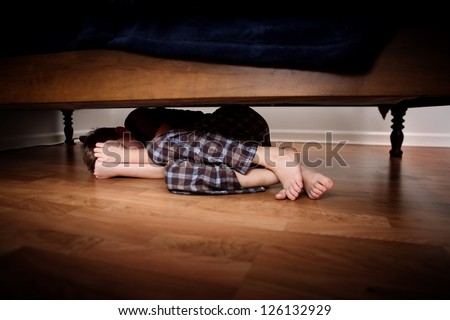 Fearful boy hiding under the bed