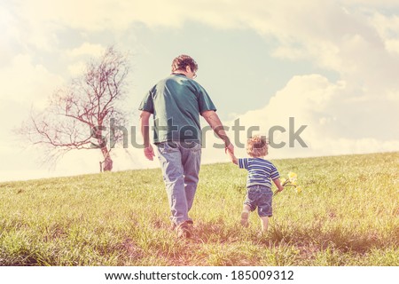 Father and son walking hand in hand up a hill in the spring