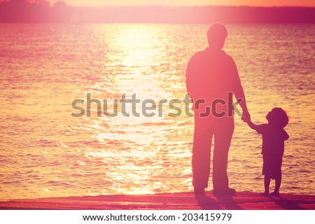Father and son on a dock at sunset boy looking up at his father Father and son on a dock at sunset boy looking up at his father