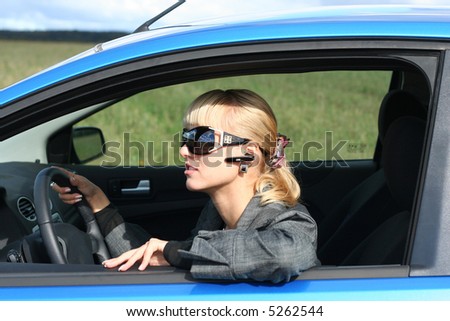 young blond woman in a blue car in sun-glasses with hands free headset