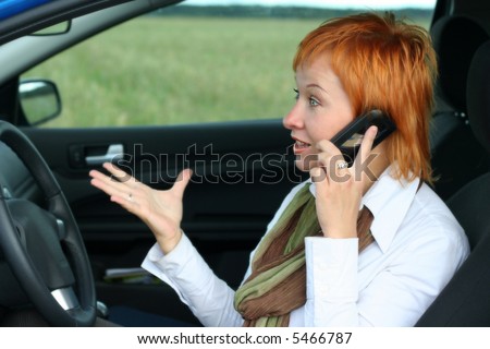Red-haired woman with mobile-phone in a car. She is fury