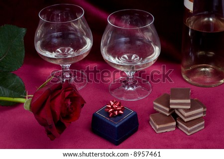 Valentine dinner with rose, gift box, candies and two glasses of white wine on purple velvet background.