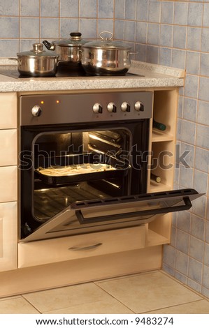 Open built-in electric oven with French fries and stainless steel cooking pots on stove.