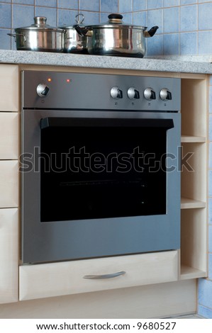 Built-in stainless steel electric oven with cooking pots on stove.