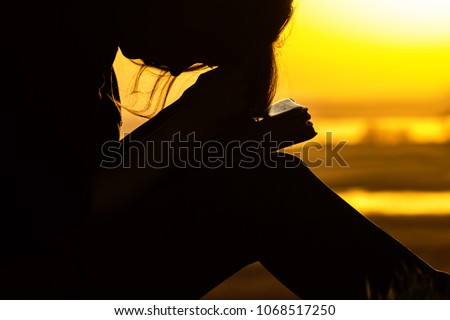 silhouette of young woman praying to God in the nature with the Bible, the girl repents of her sins, sincerely pours out feelings near the tree at sunset, the concept of religion and spirituality
