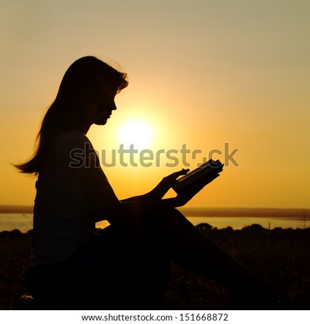 silhouette of a girl with a book in  hands at sunset