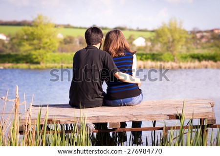 man embraces girl sitting on a pier at the river bank