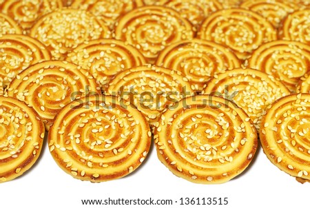 Round cookies with sesame seeds laid out in rows on a white background