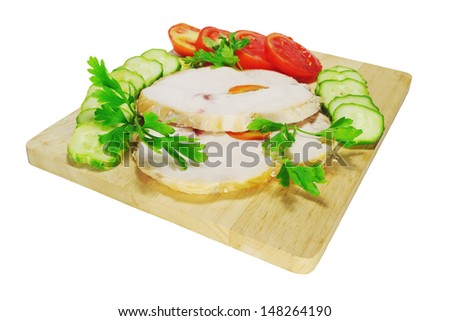 Two pieces of chicken ham with tomatoes and cucumbers on a wooden chopping board isolated on white background