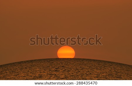 Beautiful summer sunset at sea - large bright orange sun sets over the horizon of the Black sea, Crimea