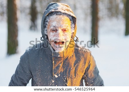 Portrait of an young frozen man with an open mouth while Jogging in a Blizzard in the woods. Face covered with snow.