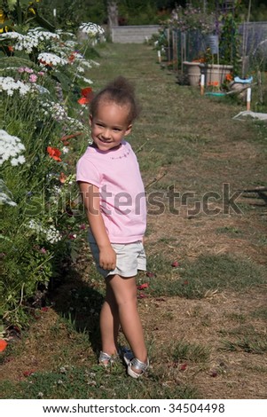 A young 2-year-old mixed-race girl enjoys the summer flower garden.