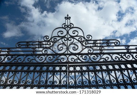 An intricate old wrought iron fence fragment against a deep blue sky with white clouds, Colorado, USA